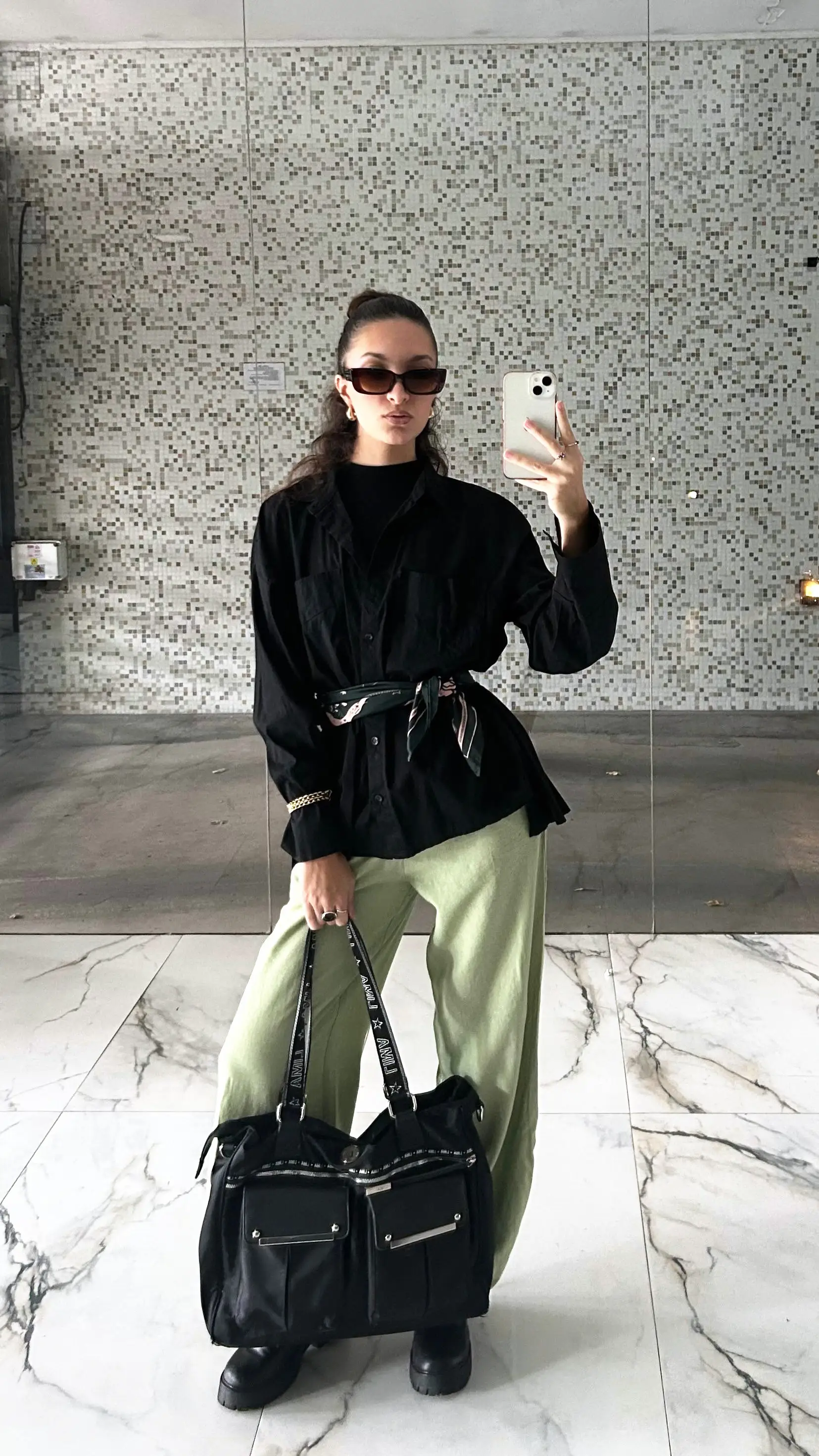 Chiara Capucci de cuerpo entero, con camisa negra y pantalón amplio verde claro.