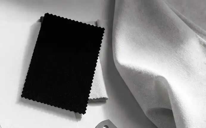 Muestra de tela negra de borde dentado sobre un textil claro.